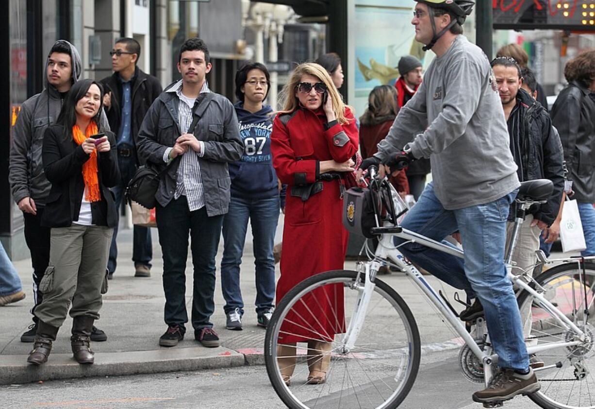 A nicely dressed woman in a red coat is surrounded by casually dressed people as they prepare to cross Stockton Street in Union Square in San Francisco on Feb. 10.