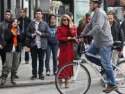 A nicely dressed woman in a red coat is surrounded by casually dressed people as they prepare to cross Stockton Street in Union Square in San Francisco on Feb. 10.