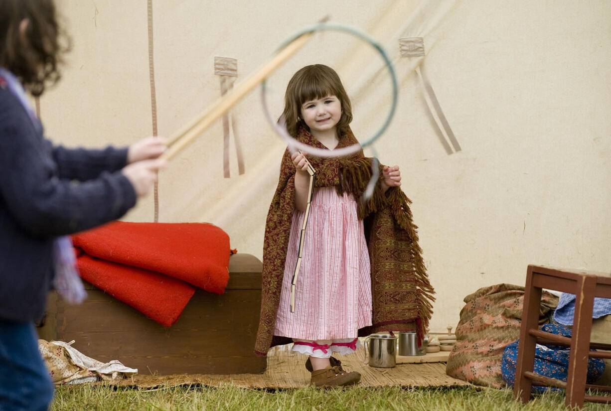 Brigade encampment re-enactor Katie McKenzie of Battle Ground, plays with a Jacob's ladder toy as others play the game of Graces with a hoop and stick at the Fort Vancouver National Historic Site in 2011.