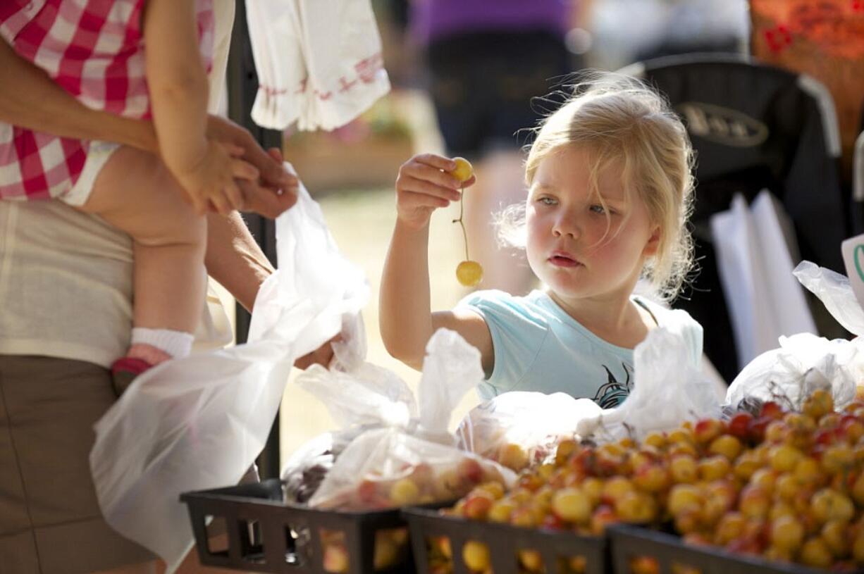 Ava Bond, shopping with her mom Alexis and sister Sawyer, uses Produce Pals tokens to buy cherries at the Salmon Creek Farmers' Market on Aug. 8.