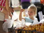 Ava Bond, shopping with her mom Alexis and sister Sawyer, uses Produce Pals tokens to buy cherries at the Salmon Creek Farmers' Market on Aug. 8.