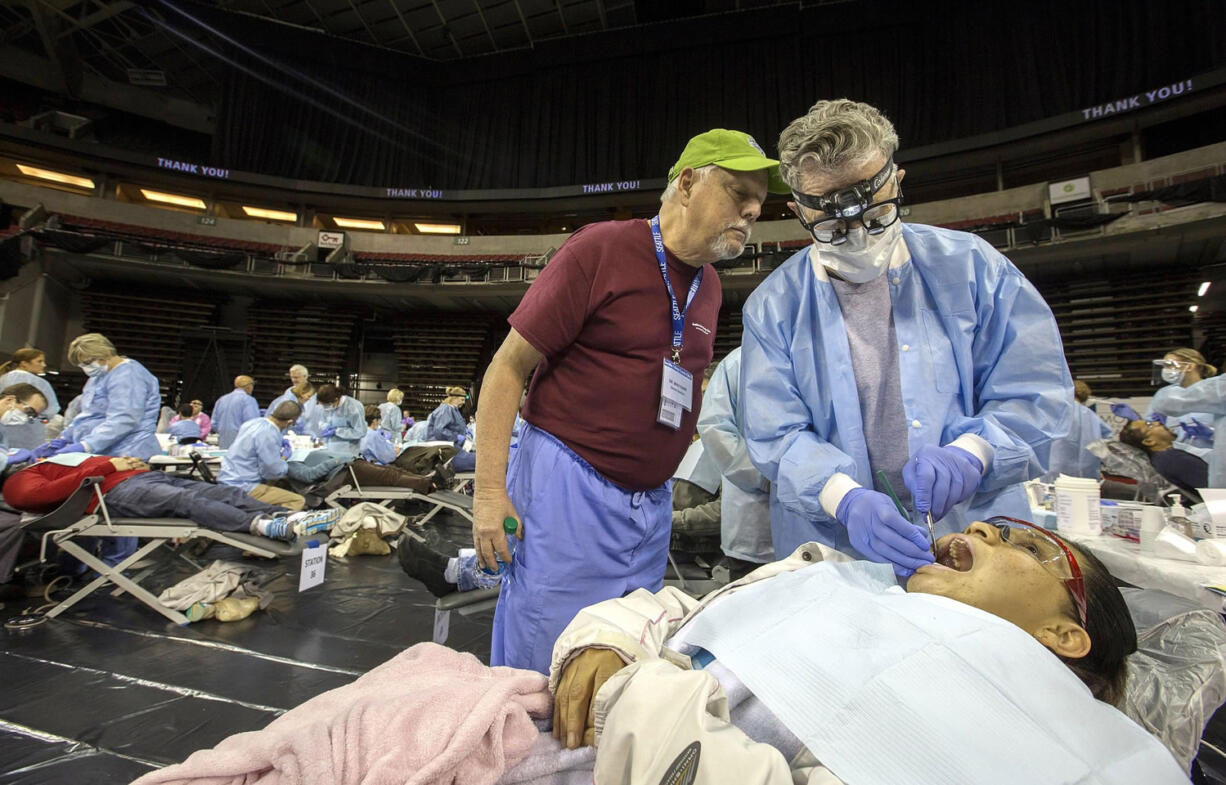 Dr. Mike Karr, left, co-director of dental clinic with Remote Area Medical, looks on as Dr. Phillips Trautman does dental work on Reyna Rosales in Seattle on October 23, 2014.