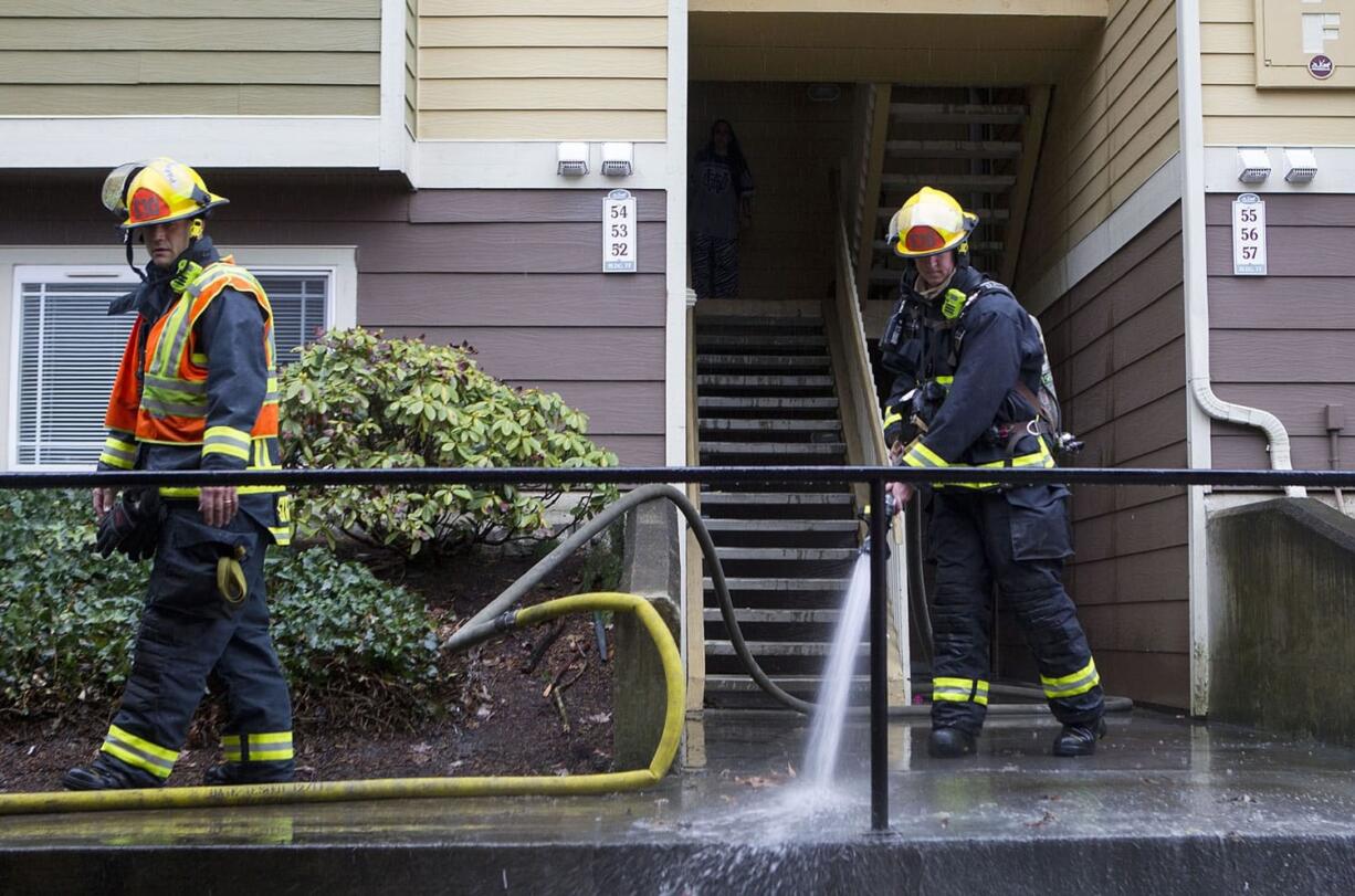 Firefighters Kevin Stromberg, left, and Joe Spatz spray down the sidewalk in front of an apartment building that caught on fire Wednesday in east Vancouver.