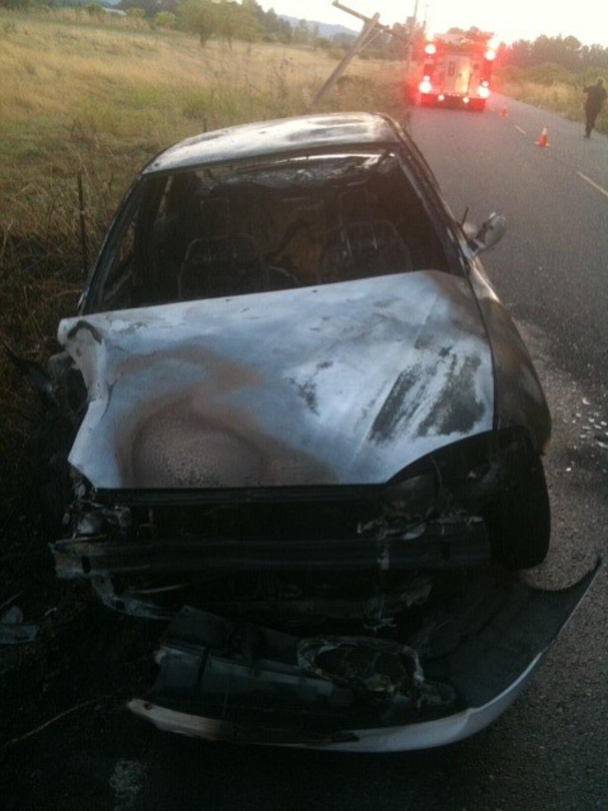 The remains of a car smolder after it crashed into a utility pole on Northwest Lower River Road early Saturday evening.