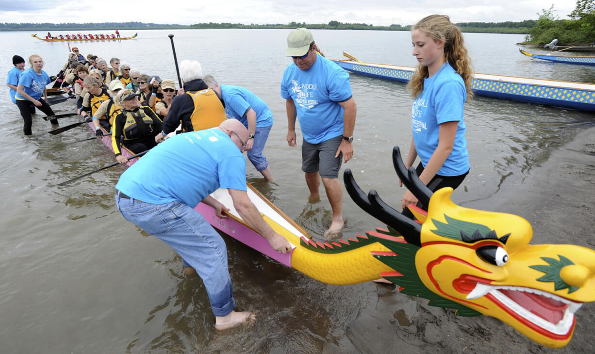 Dragon boat racers are assisted by volunteers in blue tees, including Grace Newcomb, right, as they paddle to shore during the third annual Paddle for Life Dragon Boat Festival on Saturday at Vancouver Lake.