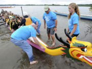 Dragon boat racers are assisted by volunteers in blue tees, including Grace Newcomb, right, as they paddle to shore during the third annual Paddle for Life Dragon Boat Festival on Saturday at Vancouver Lake.