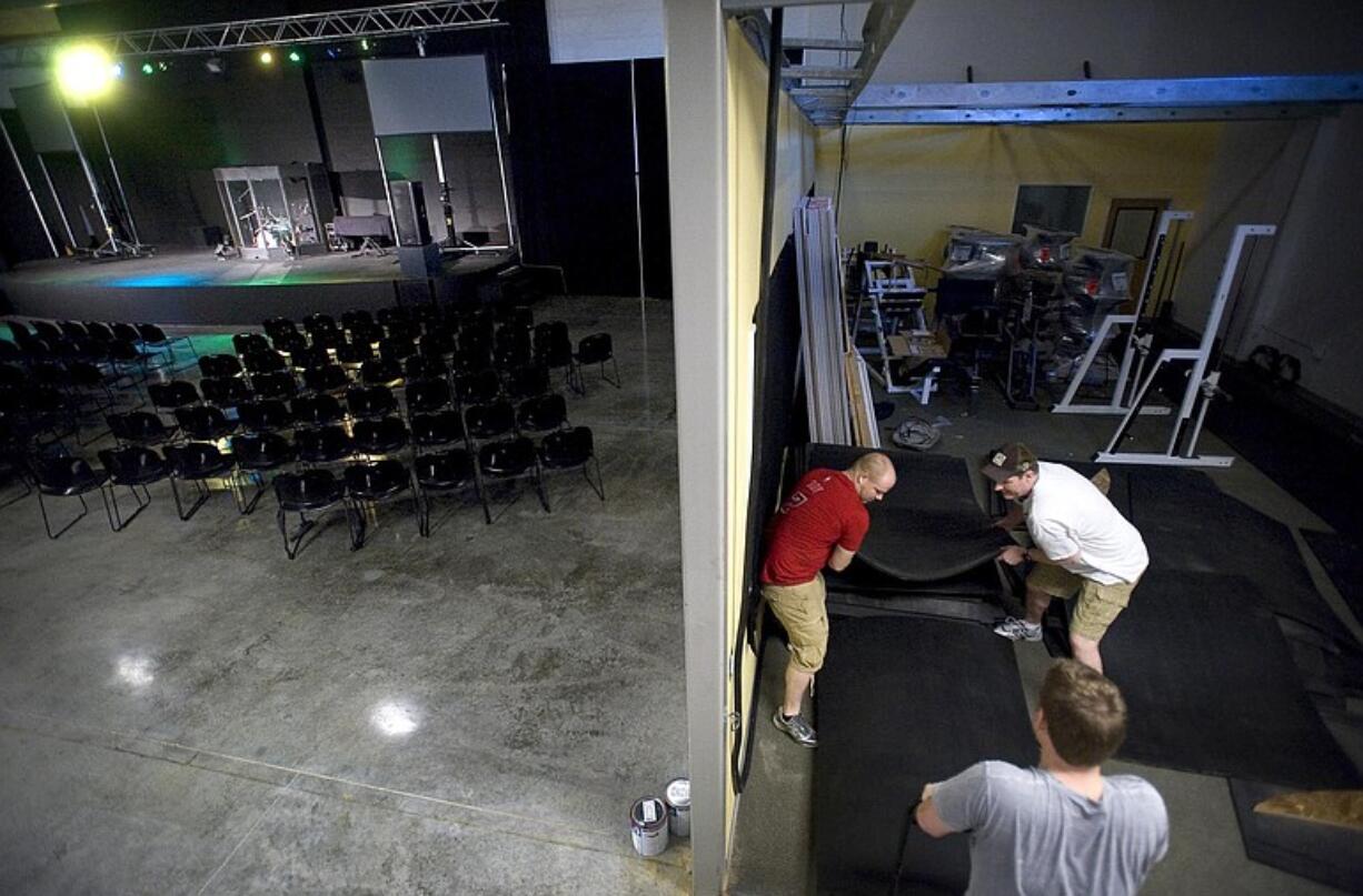 Kessid Church Youth Pastor Chris Potter, clockwise from top left, Kessid Center General Manager Keith Walther and Kessid Church Lead Pastor Danny Clinton pull rubber mats from a storage area near a stage Saturday in preparation for the opening of the Kessid Center, a nonprofit community center, in the same space that housed the now defunct Bally Total Fitness center in Fishers Landing.