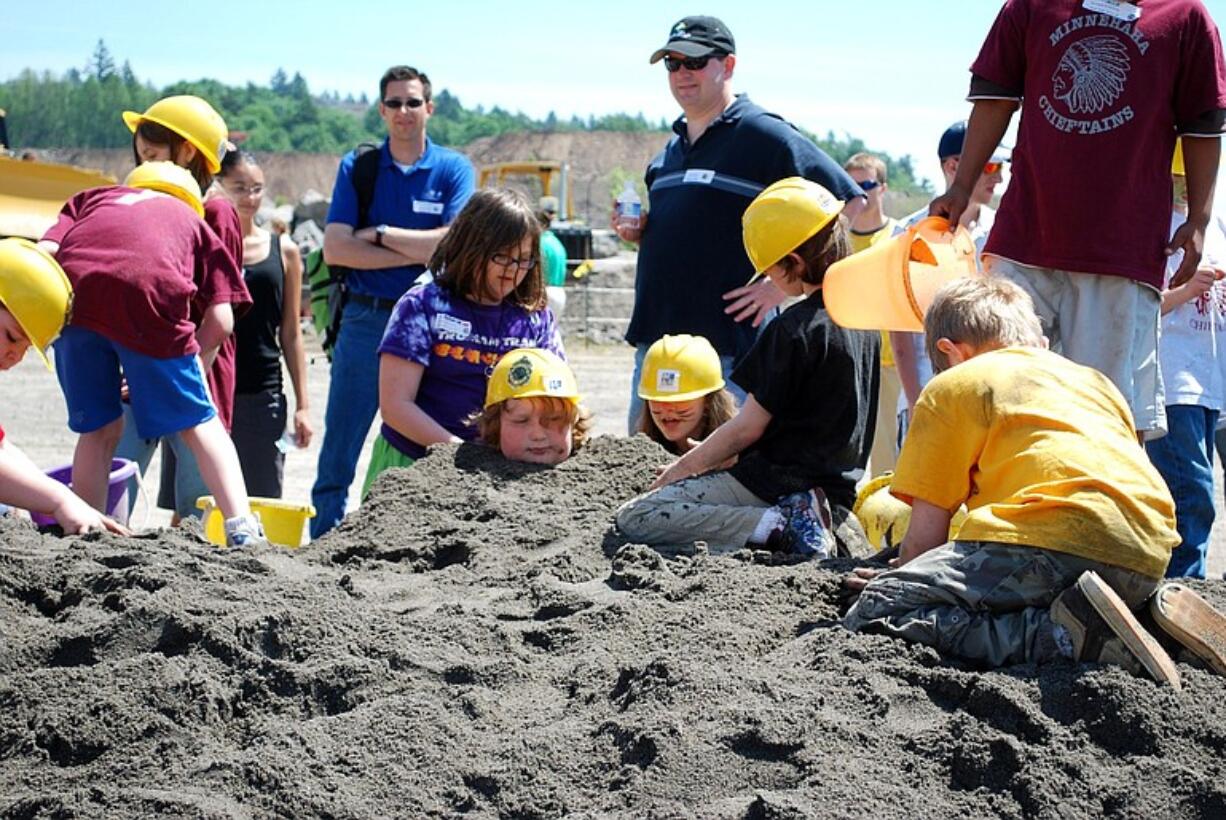 A few elementary students take a break from games and heavy equipment operation to play in the sand.