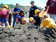 A few elementary students take a break from games and heavy equipment operation to play in the sand.