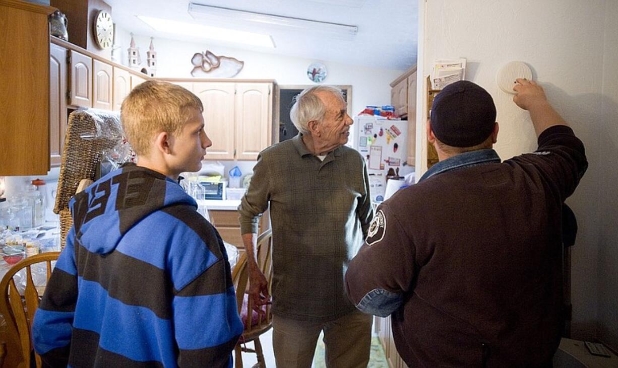 Firefighter Shawn Richey of Fire District 6, right, assisted by Paydenn Paull-Weston, left, replaces a smoke detector battery Saturday in the home of Stan Coleman, center, in Meadow Verde Mobile Home Park in Hazel Dell.