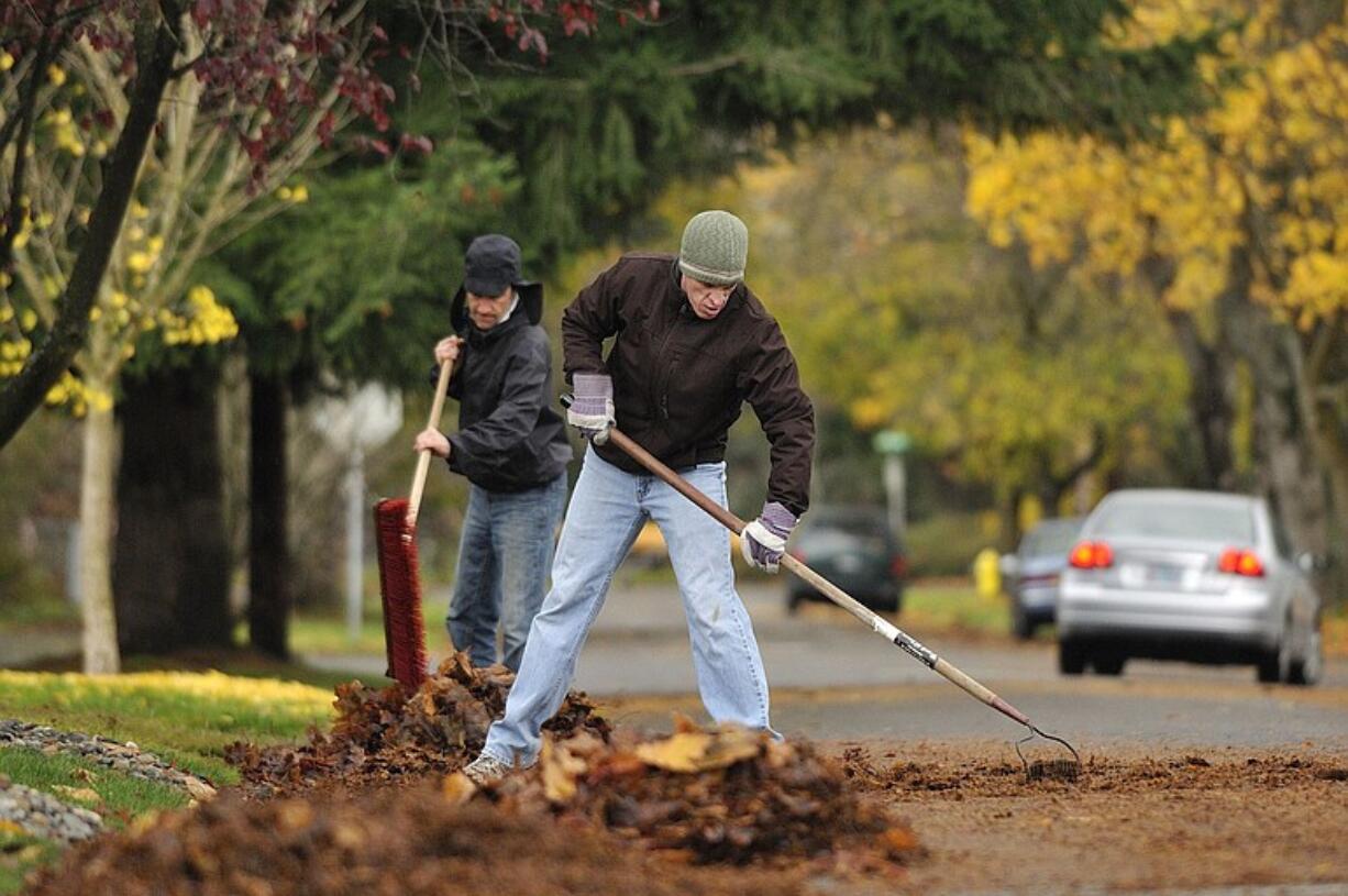 Neighbors Mark Harms, left, and Alan Wilson clear leaves from the road in front of their homes Thursday in the Hough neighborhood in Vancouver.