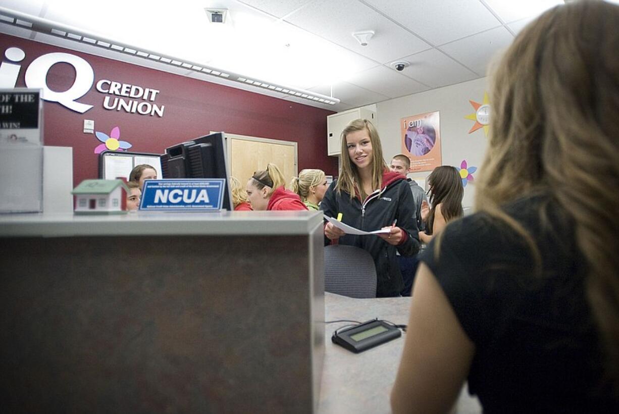 Camas High School sophomore Kathryn Johnson, 16, helps a student make a deposit at the campus iQ Credit Union.