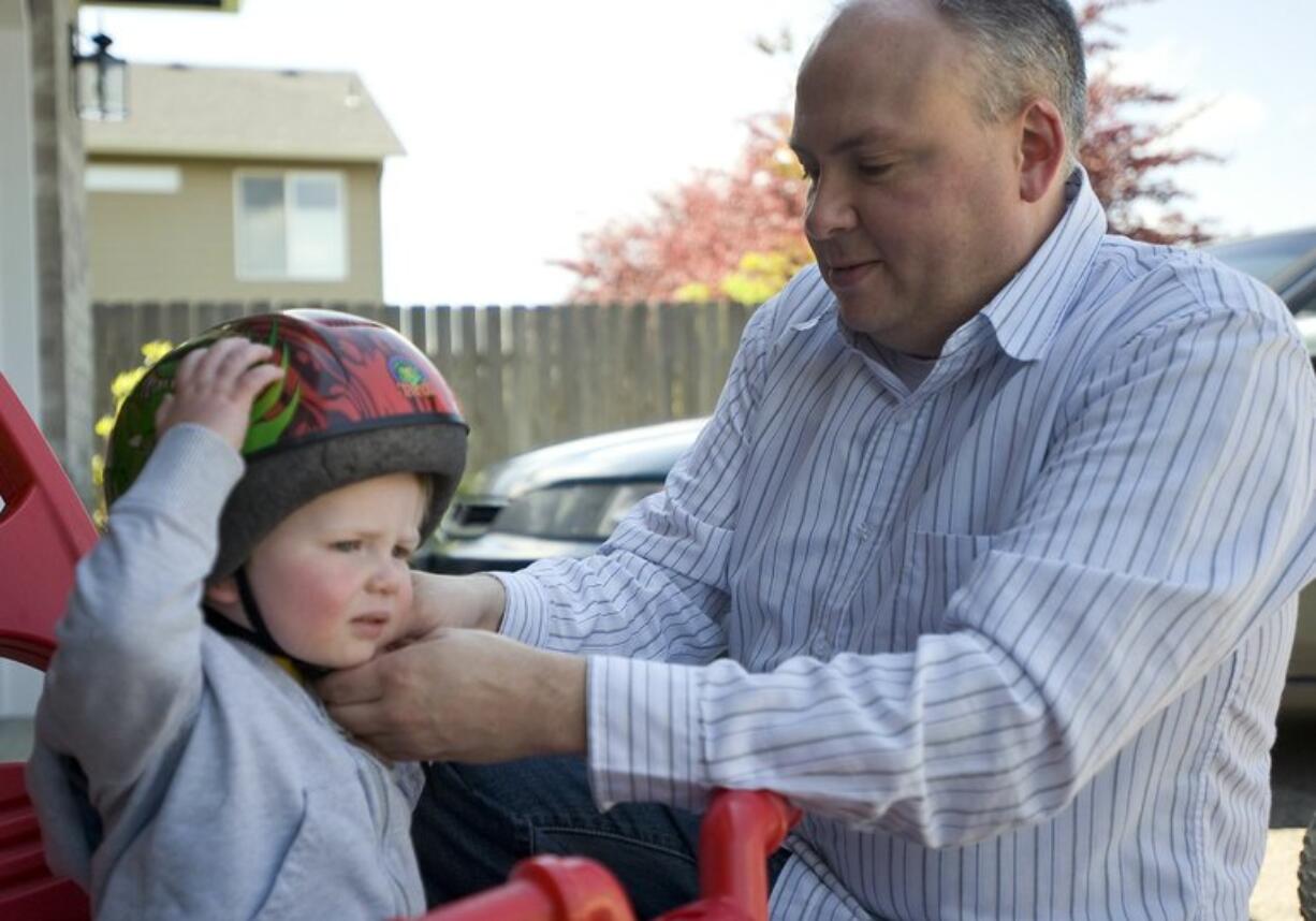 Jerry Gowen earned his MBA degree this year after four years of night classes at Washington State University Vancouver. Here, he straps a helmet on his son, Scott, 20 months old, outside his Felida home.