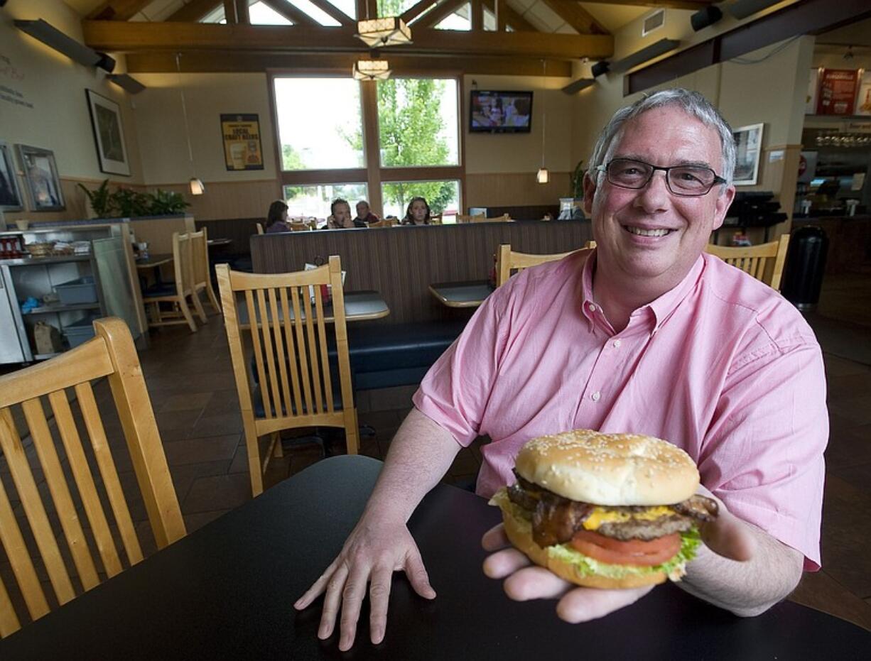 Burgerville President and CEO Jeff Harvey shows off one of the company's signature menu items, the Half-Pound Colossal cheeseburger with bacon at the company's Salmon Creek restaurant.