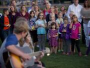 Photos by Steven Lane/The Columbian
Classmates, teachers and friends listen to a rendition of Ben Harper's song &quot;Waiting on an Angel&quot; on Wednesday evening at a vigil for Stormy Solis at Fisher's Basin Community Park in east Vancouver. The 7-year-old girl died from a brain injury after reportedly falling off a swing at Fisher's Landing Elementary School.  At top, a picture of Stormy on display at the vigil.