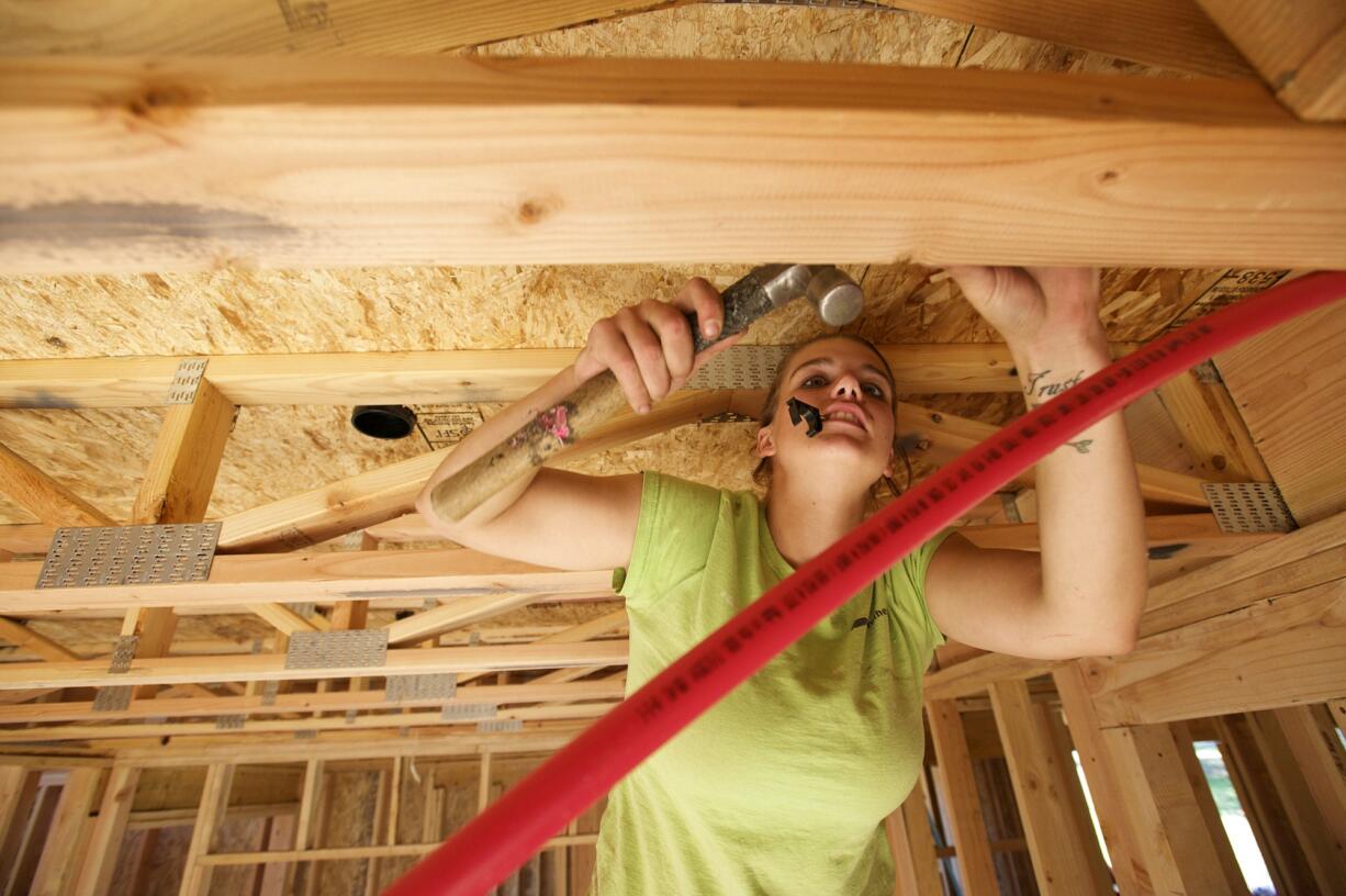 Smokey Fritz, apprentice plumber, grips a plastic pipe fitting in her mouth as she climbs a ladder to install plumbing in a new home under construction in Camas. Fritz likely is the only woman plumber in Clark County.