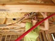 Smokey Fritz, apprentice plumber, grips a plastic pipe fitting in her mouth as she climbs a ladder to install plumbing in a new home under construction in Camas. Fritz likely is the only woman plumber in Clark County.