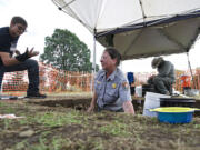 Portland State University student Tyler Molter, from left, takes an artifact Tuesday from National Park Service archeologist Beth Horton during excavation of a flag pole site on the Parade Ground at Vancouver Barracks.