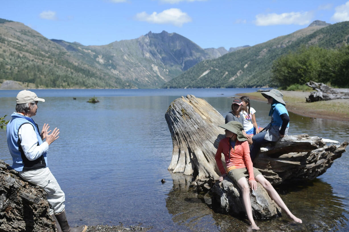 Leaning against a blown-down tree on the banks of Coldwater Lake, Cynthia Gardner, a U.S. Geological Survey research geologist, weaves the story of the May 18, 1980 eruption of Mount St. Helens. Middle school girls settle on a tree stump in the lake listen.