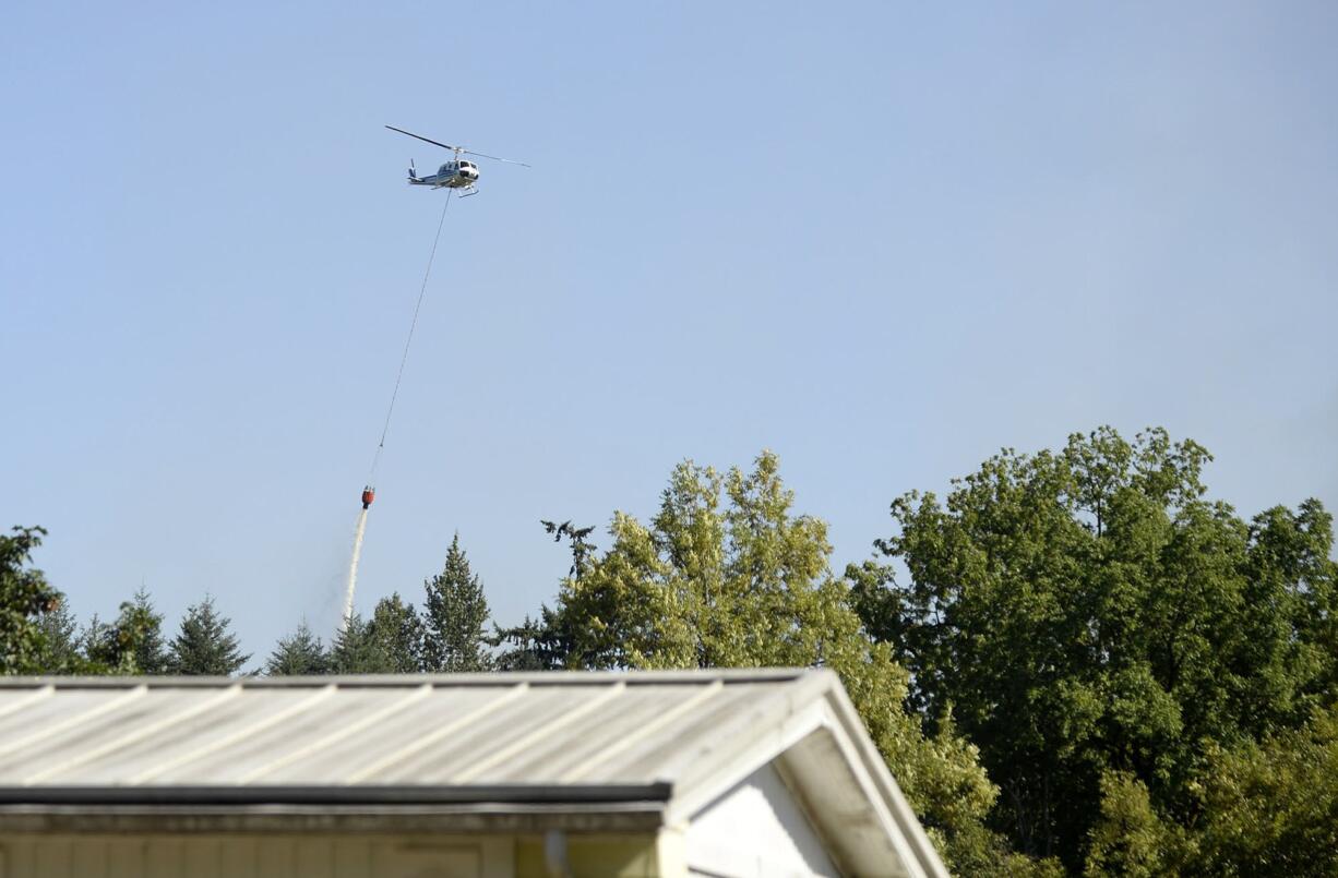 A helicopter helps extinguish a fire in a wooded area near homes along Northeast 81st Avenue on Tuesday afternoon.