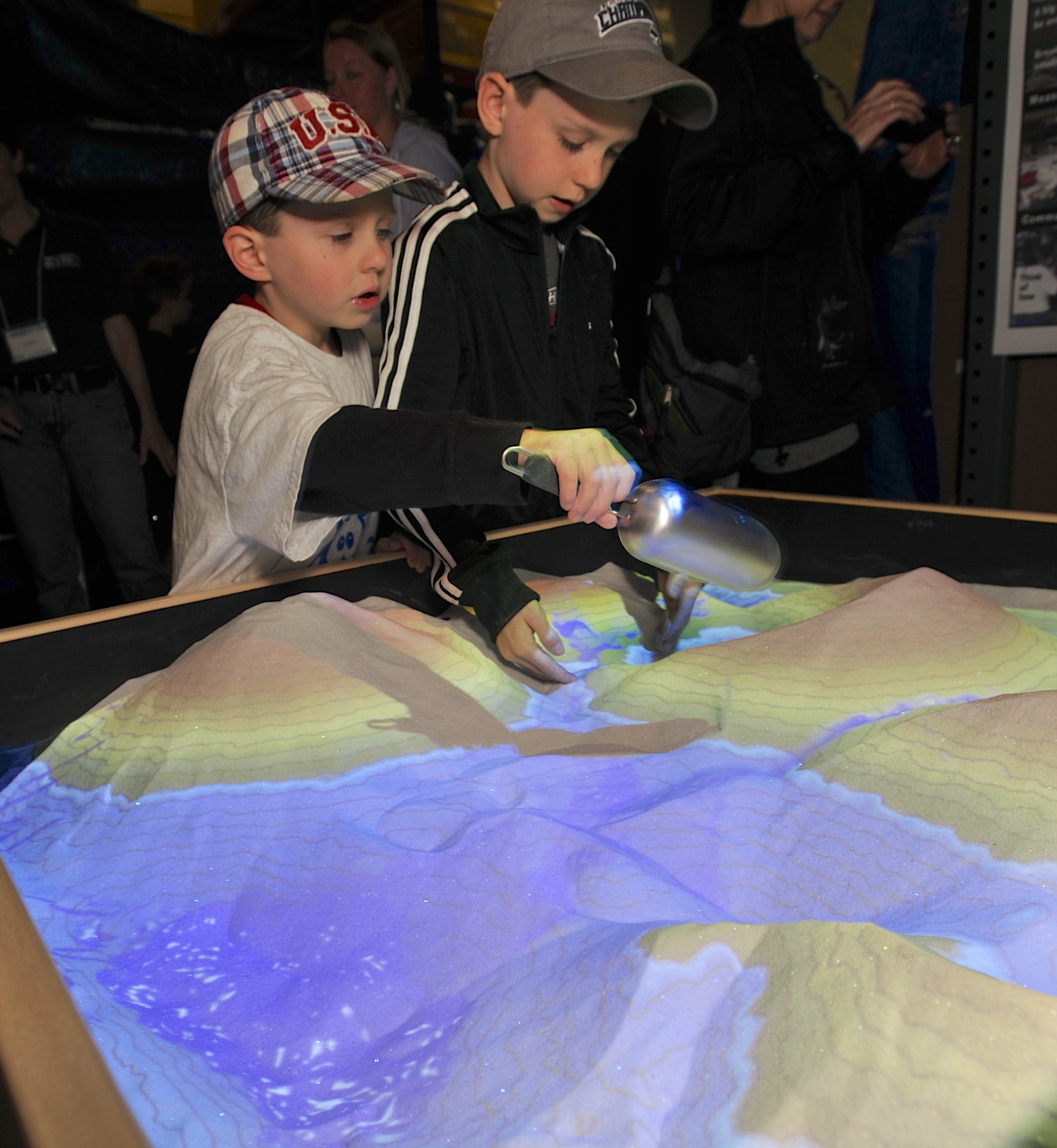 Aaron, left, and Alex Erickson play in an augmented reality sandbox, which projects topography contours on shifting sand piles, during the U.S.