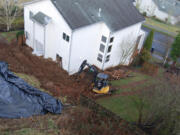 An excavator operator clears dirt away Wednesday from the back of John Trost's home in Camas.