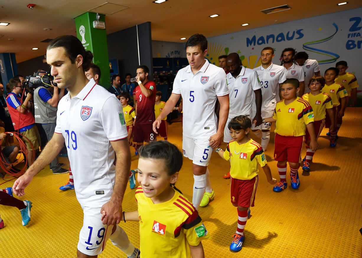 Mallory Stonier, 9, walks onto the field at the World Cup in Manaus, Brazil, with Team USA player Graham Zusi.