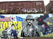 Artist Guy Drennan, at lower left, works Tuesday on a mural honoring Korean War veterans on Vancouver's Remembrance Wall.