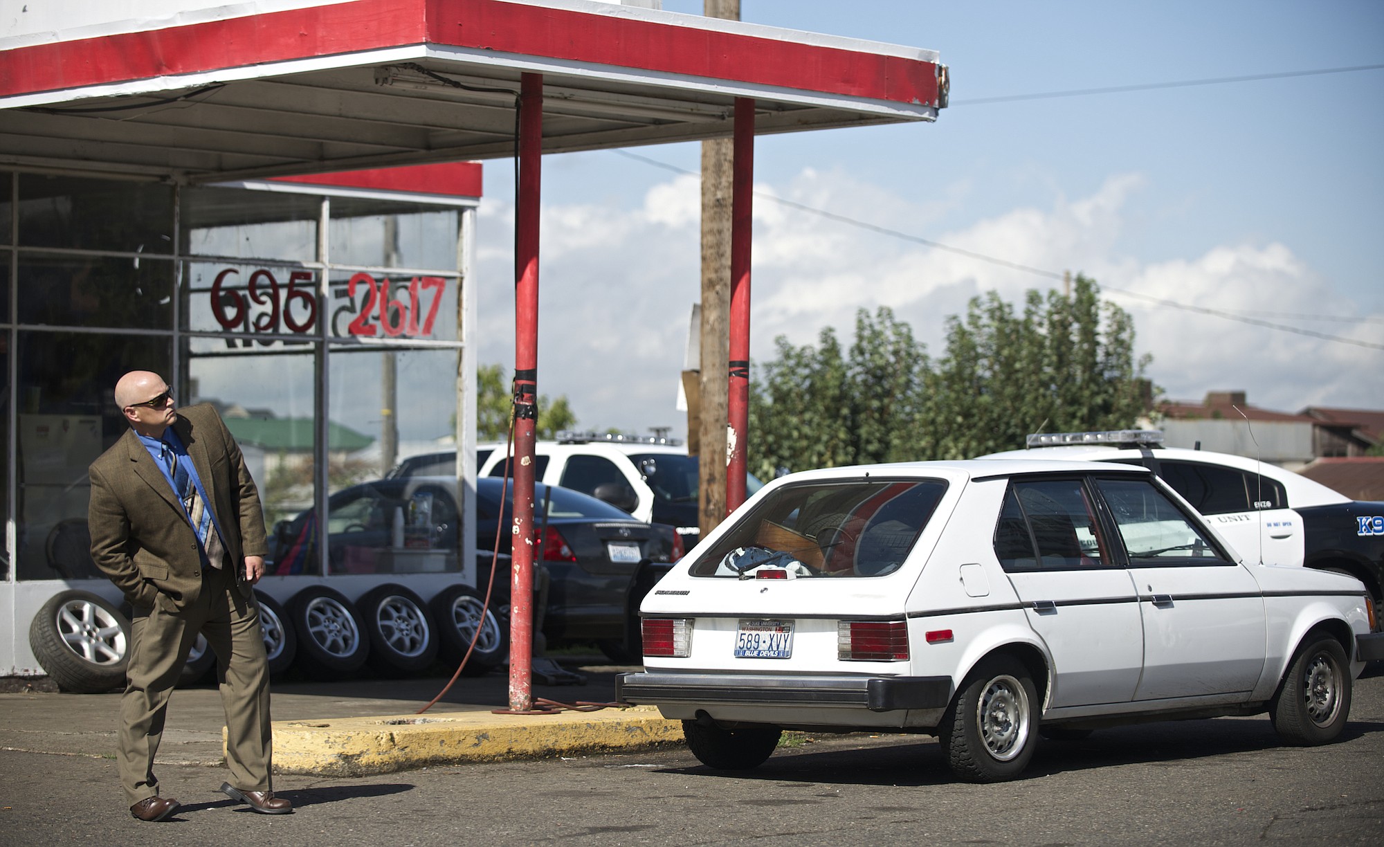 A plain-clothes police officer stands in the parking lot of The Tire Place at Fourth Plain Boulevard and Kauffman Avenue next to a white Dodge which is believed to belong to a suspect in Wednesday's fatal stabbing.