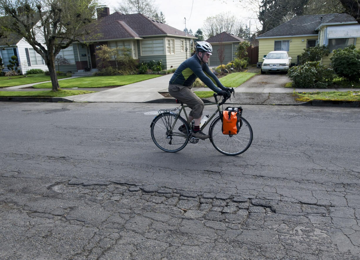 A cyclist pedals past a damaged section of Columbia Street in Vancouver in late March. The Commission on Street Funding was asked to issue a recommendation by mid-summer in case the City Council wanted to put a funding measure on November's ballot as part of the overall approach to road repairs.