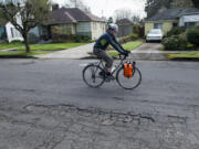 A cyclist pedals past a damaged section of Columbia Street in Vancouver in late March. The Commission on Street Funding was asked to issue a recommendation by mid-summer in case the City Council wanted to put a funding measure on November's ballot as part of the overall approach to road repairs.