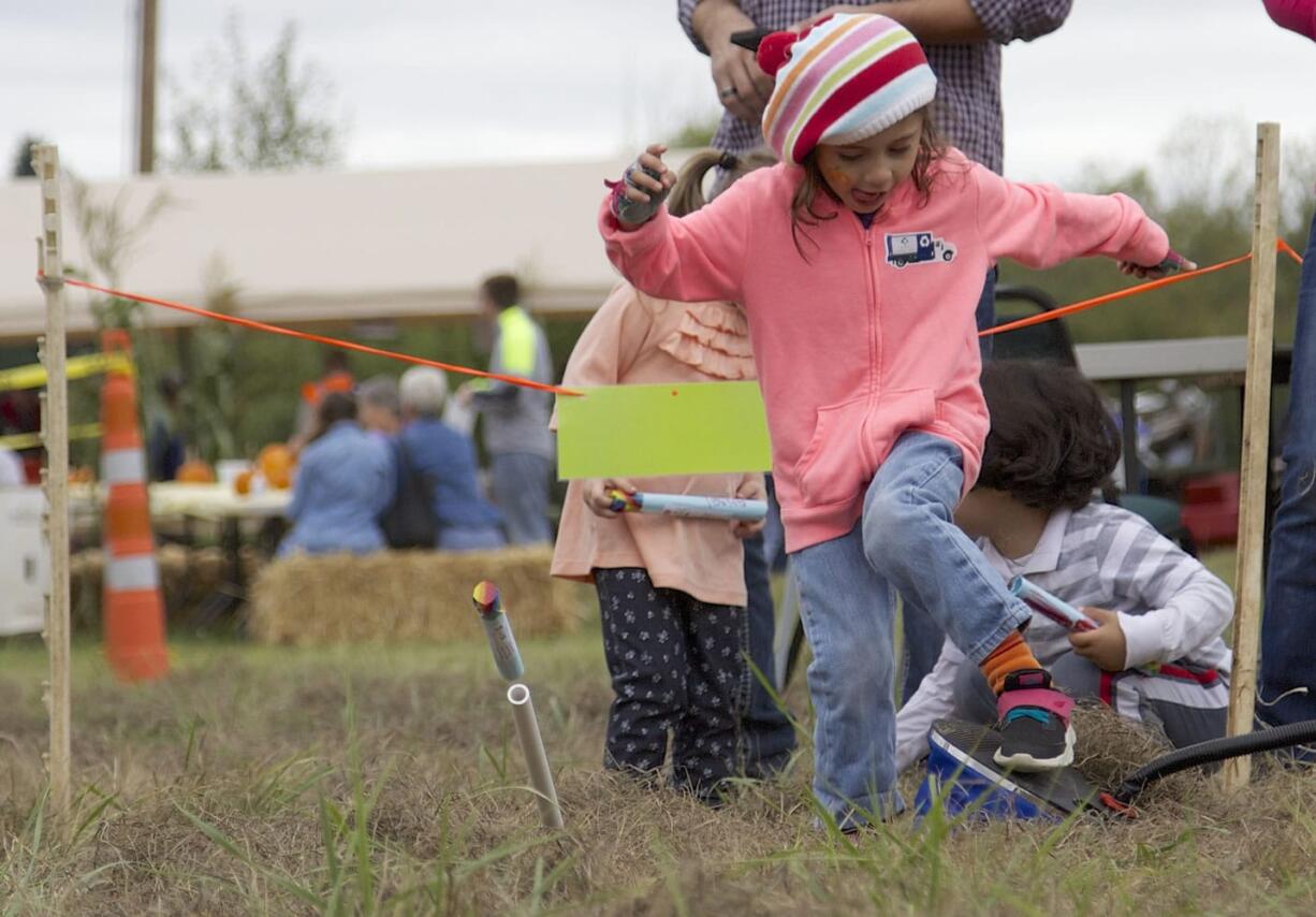 LiliAhna Schlitt, 4, steps on a pump to use compressed air to launch a handmade rocket Saturday at the Harvest Fun Days.