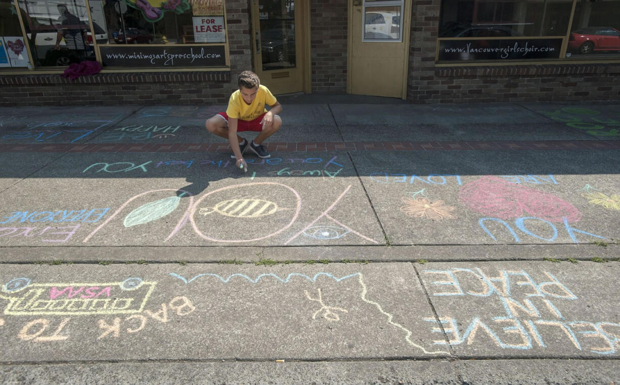 Lukas Miller writes messages in chalk Tuesday on a sidewalk in downtown Vancouver.