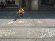 Lukas Miller writes messages in chalk Tuesday on a sidewalk in downtown Vancouver.