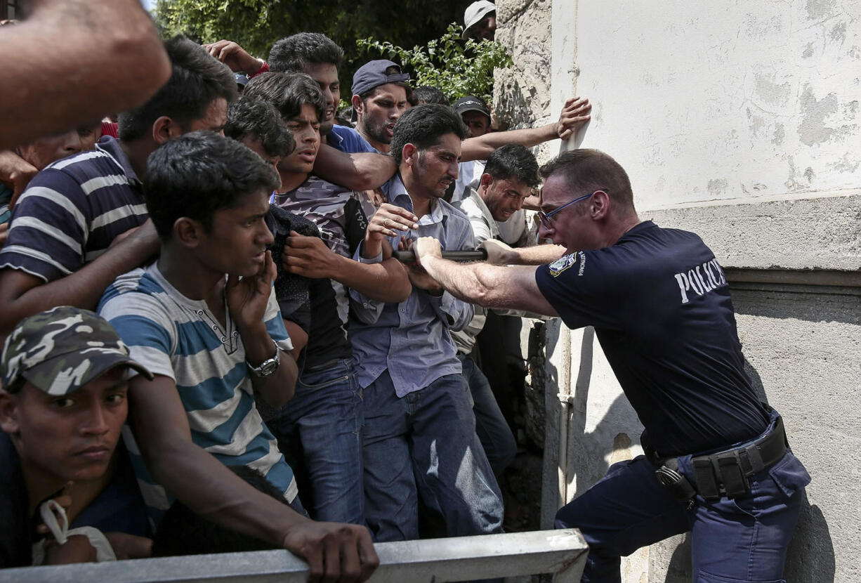 A Greek policeman tries to hold migrants behind a fence Monday as they wait for a registration procedure outside a police station on the southeastern island of Kos.