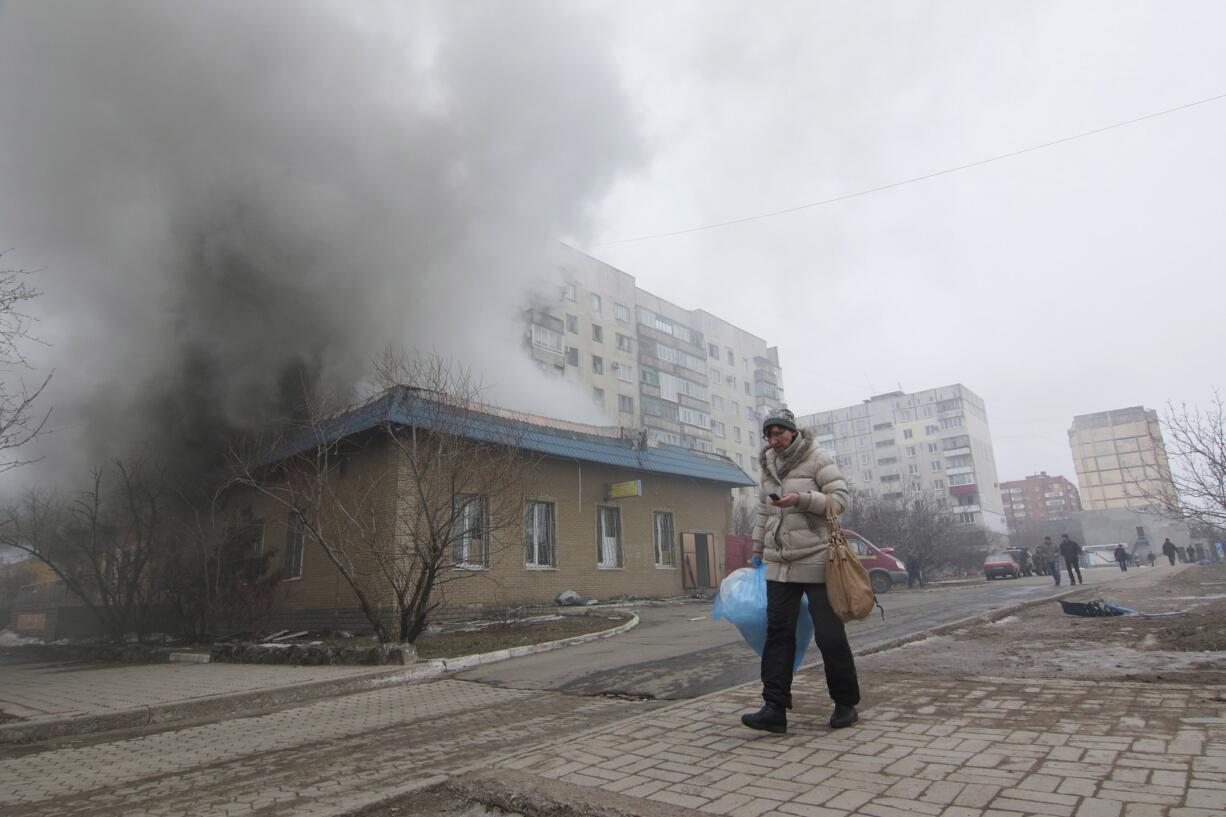 A woman resident passes by a burning house in Mariupol, Ukraine, Saturday, Jan. 24, 2015. A crowded open-air market in Ukraine's strategically important coastal city of Mariupol came under rocket fire Saturday morning, killing at least 10 people, regional police said. Heavy fighting in the region in the autumn raised fears that Russian-backed separatist forces would try to establish a land link between Russia and Crimea. Pro-Russian separatist forces have positions within 10 kilometers (six miles) from Mariupol's eastern outskirts.