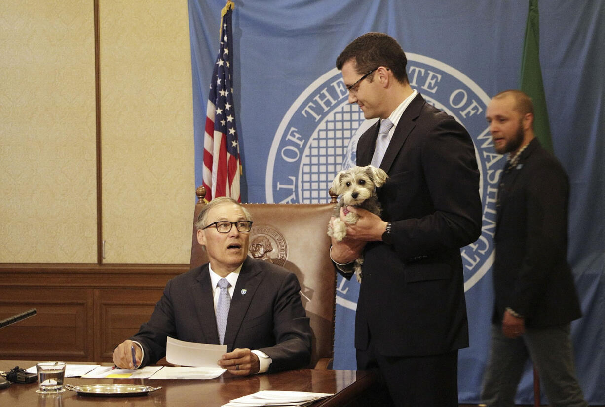 Sen. Joe Fain holds his dog, Waffles, as Gov. Jay Inslee, seated, prepares to sign a bill expanding the state's animal cruelty laws, Monday in Olympia.