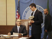 Sen. Joe Fain holds his dog, Waffles, as Gov. Jay Inslee, seated, prepares to sign a bill expanding the state's animal cruelty laws, Monday in Olympia.