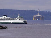 A Washington state ferry sails in view of the oil drilling rig Polar Pioneer and a handful of kayakers while being towed toward a dock Thursday, May 14, 2015, in Seattle. The rig is the first of two drilling rigs Royal Dutch Shell is outfitting for oil exploration and was towed to the Port of Seattle site despite the city's warning that it lacks permits and threats by kayaking environmentalists to paddle out in protest.