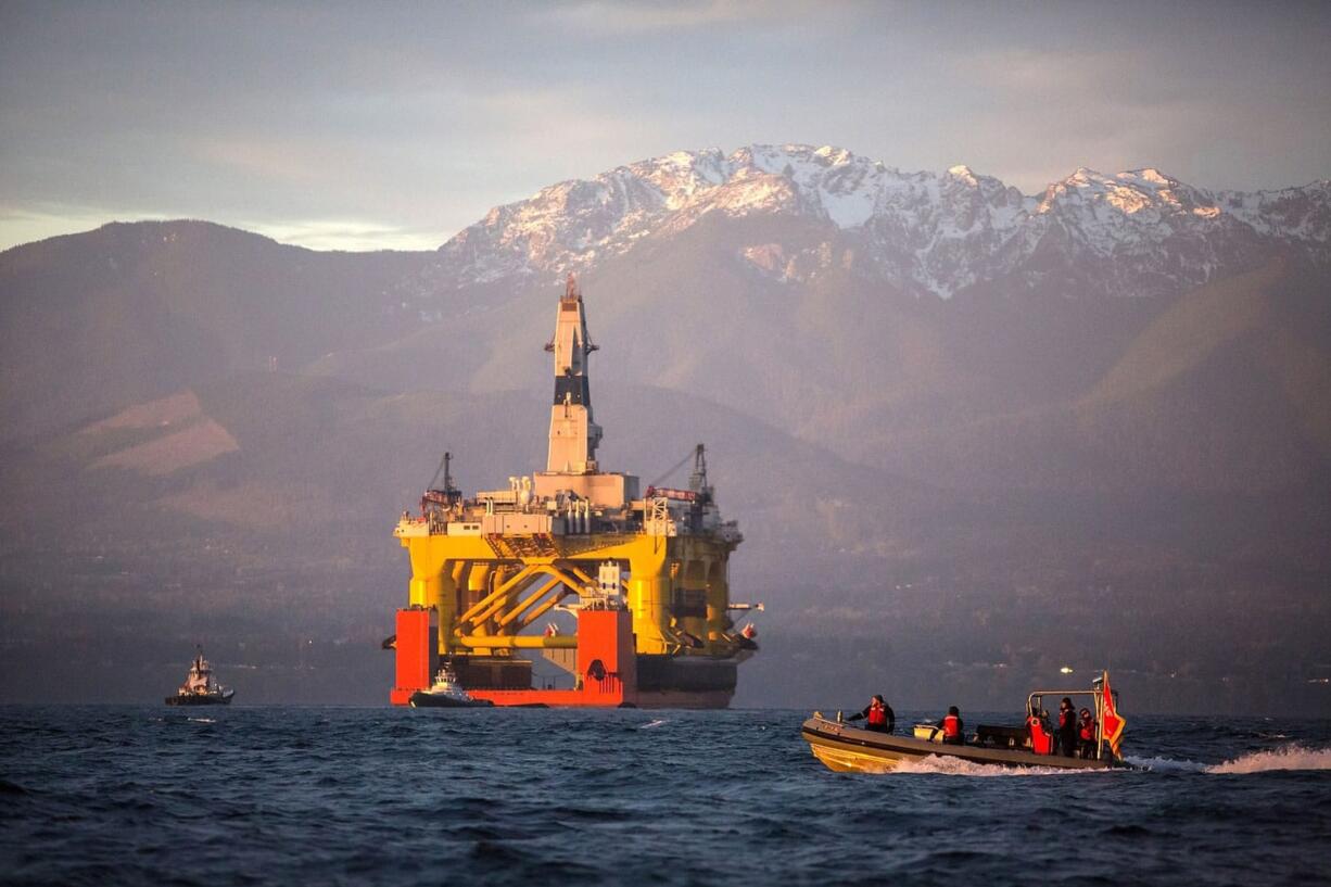 With the Olympic Mountains in the background, a small boat crosses in front of an oil drilling rig as it arrives in Port Angeles aboard a transport ship after traveling across the Pacific.