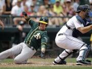 Oakland Athletics' Jed Lowrie, left, scores as Seattle Mariners catcher Mike Zunino waits for the ball in the fifth inning of a baseball game Sunday, July 13, 2014, in Seattle.