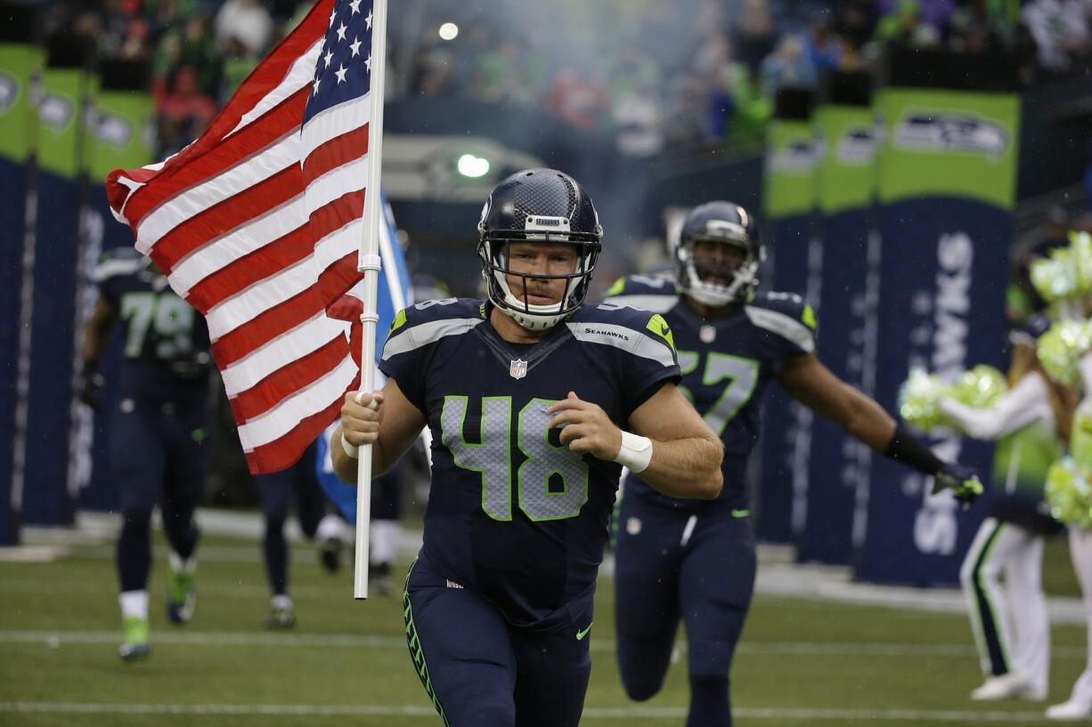 Seattle Seahawks long snapper and military veteran Nate Boyer runs out of the tunnel with a U.S. flag at the start of a preseason game against the Denver Broncos, Friday, Aug. 14, 2015, in Seattle.