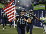 Seattle Seahawks long snapper and military veteran Nate Boyer runs out of the tunnel with a U.S. flag at the start of a preseason game against the Denver Broncos, Friday, Aug. 14, 2015, in Seattle.