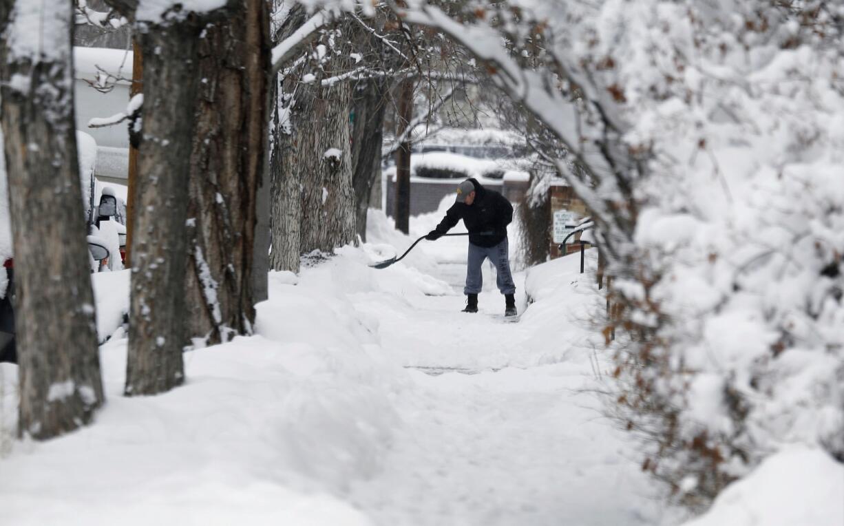 Framed by trees, a shoveler toils on a sidewalk after a winter storm sent temperatures plunging to single-digit levels and dumped up to a foot of snow Sunday in Denver.