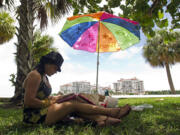 Associated Press files
A woman listens to music on her iPad as she sits in the shade at South Pointe Park in Miami Beach, Fla. Beachgoers probably have to crank up the brightness on tablets and phones to overcome all that glare in direct sunlight. Portable power packs powerful enough to charge tablets start at $100.