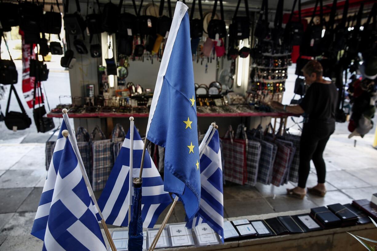 A woman adjusts items outside a kiosk Sunday in Piraeus, near Athens, Greece.