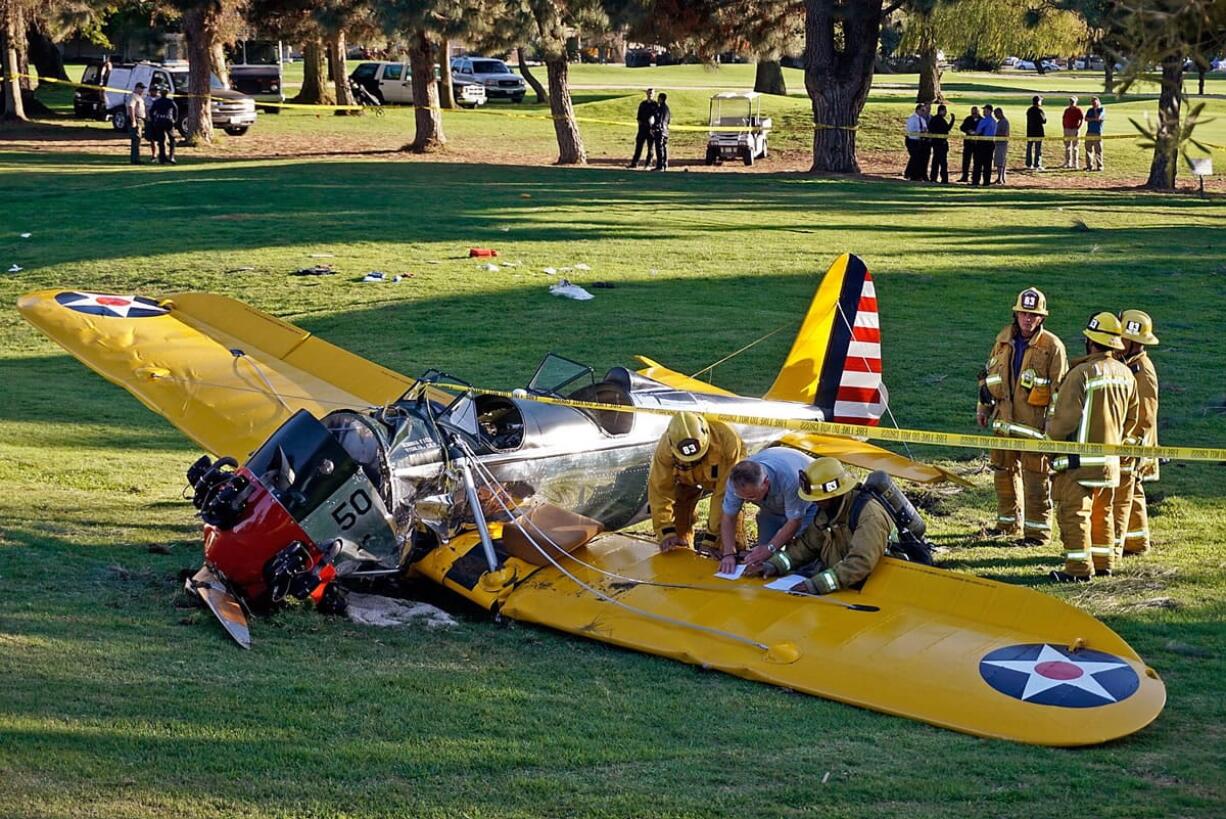 Officials work on the scene of a vintage airplane that crash-landed March 5 on the Penmar Golf Course in the Venice area of Los Angeles. Federal safety investigators have concluded that a problem with a carburetor part led to engine failure and the crash of the vintage airplane piloted by actor Harrison Ford in California. The National Transportation Safety Board said Thursday that the part known as a main metering jet likely came loose over the years since the plane was restored.