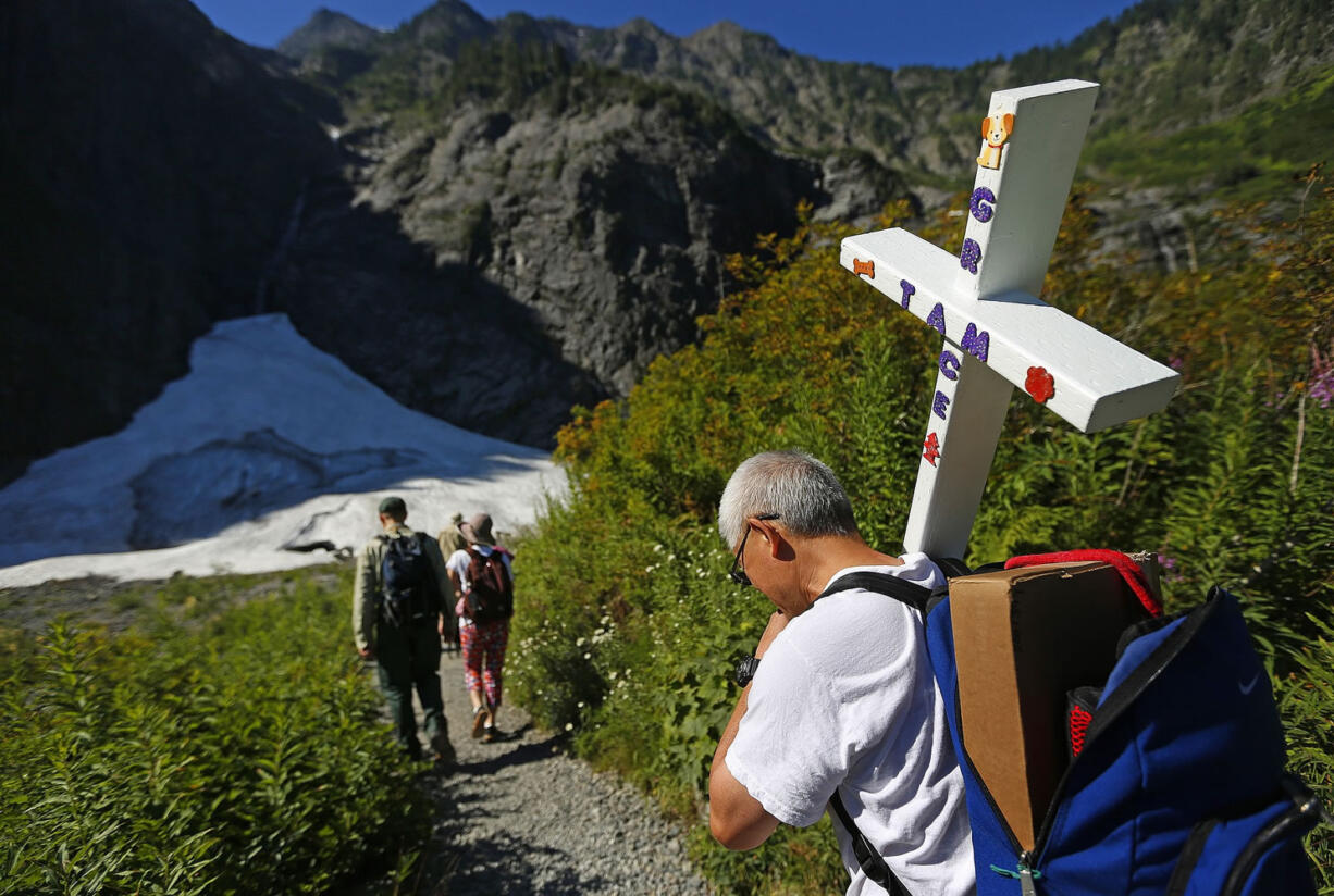 John Tam carries a cross bearing the name of his daughter, Grace, as he hikes the mile to the Big Four ice caves Thursday in Verlot, where Grace, 11, died July 31, 2010, from internal injuries after a piece of ice fell on her. Tam tried to auger the cross into the ground but the rocky spot was too stubborn; he plans to return another day to finish the job. One lavender cross already marks the spot.