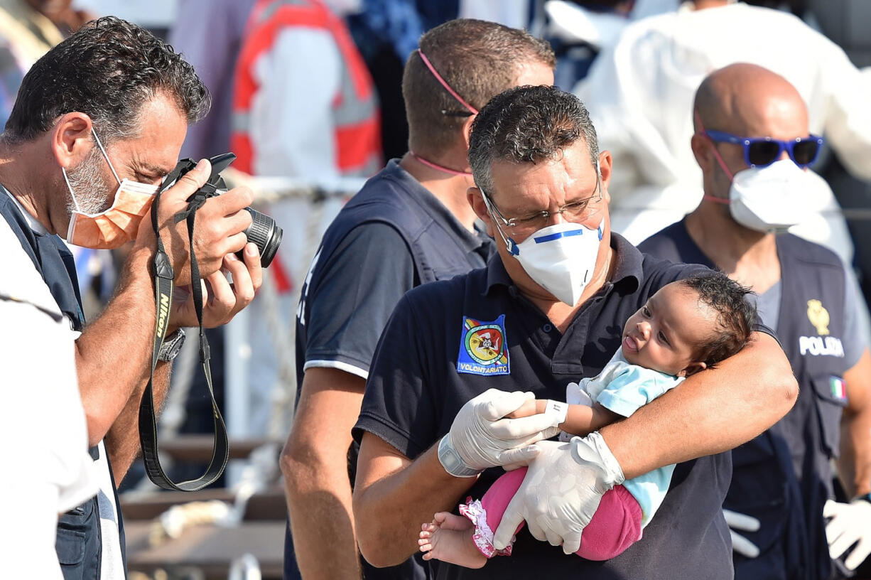 An Italian officer takes a photo of a baby as migrants disembark Friday from the Italian Coast Guard ship Fiorillo in the harbor of Pozzallo, near Ragusa, Sicily, Italy. On Thursday, 381 people were saved by the Italian coast guard before their boat sank off the Libyan coast.