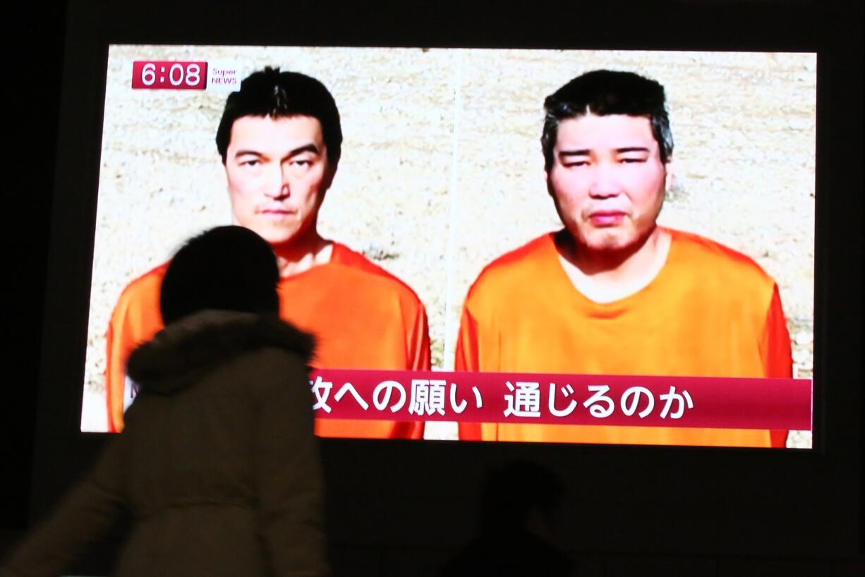 A passer-by in Tokyo watches a TV news program Friday reporting on two Japanese hostages, Kenji Goto, left, and Haruna Yukawa, held by the Islamic State group. Militants affiliated with the Islamic State group have posted an online warning that the &quot;countdown has begun&quot; for the group to kill the pair.